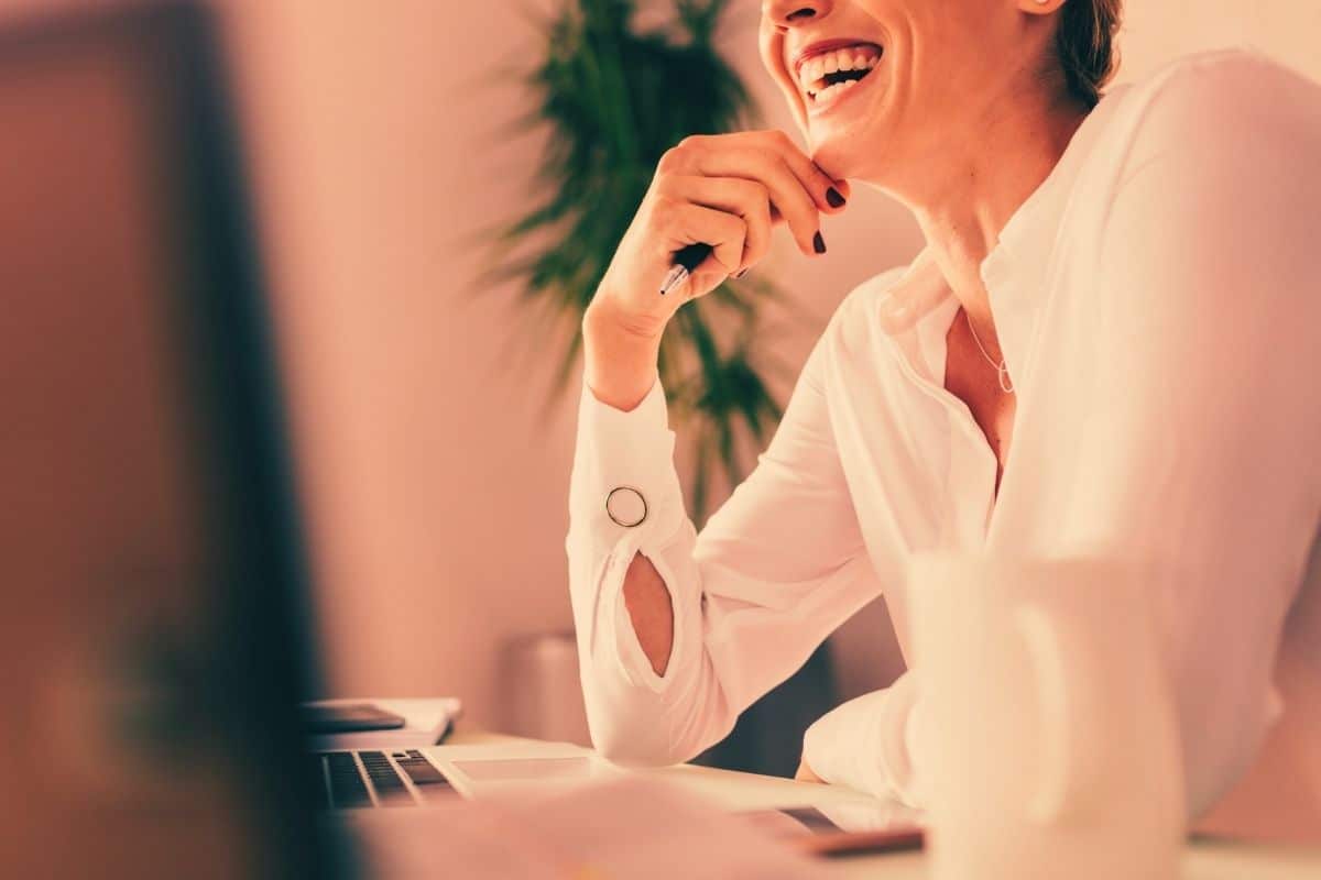 Professional woman sitting at office desk smiling wearing a white button shirt