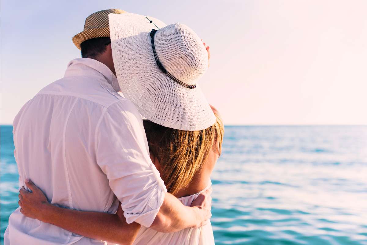 couple on the water holding each other's back and kissing behind the brim of woman's beach hat