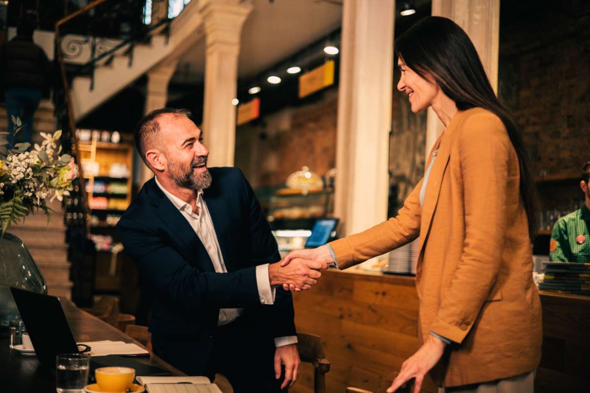 man sitting a bar and shaking a woman's hand as she approaches hims