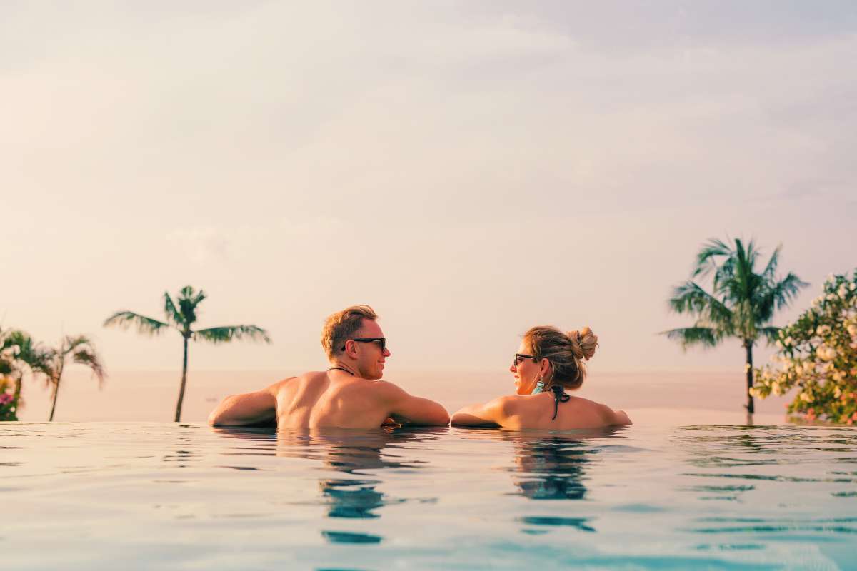 heterosexual couple relaxing in a pool at sunset and looking at each other wearing sunglasses