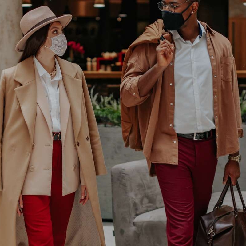 woman and man walking out of hotel lobby wearing face masks and carrying luggage