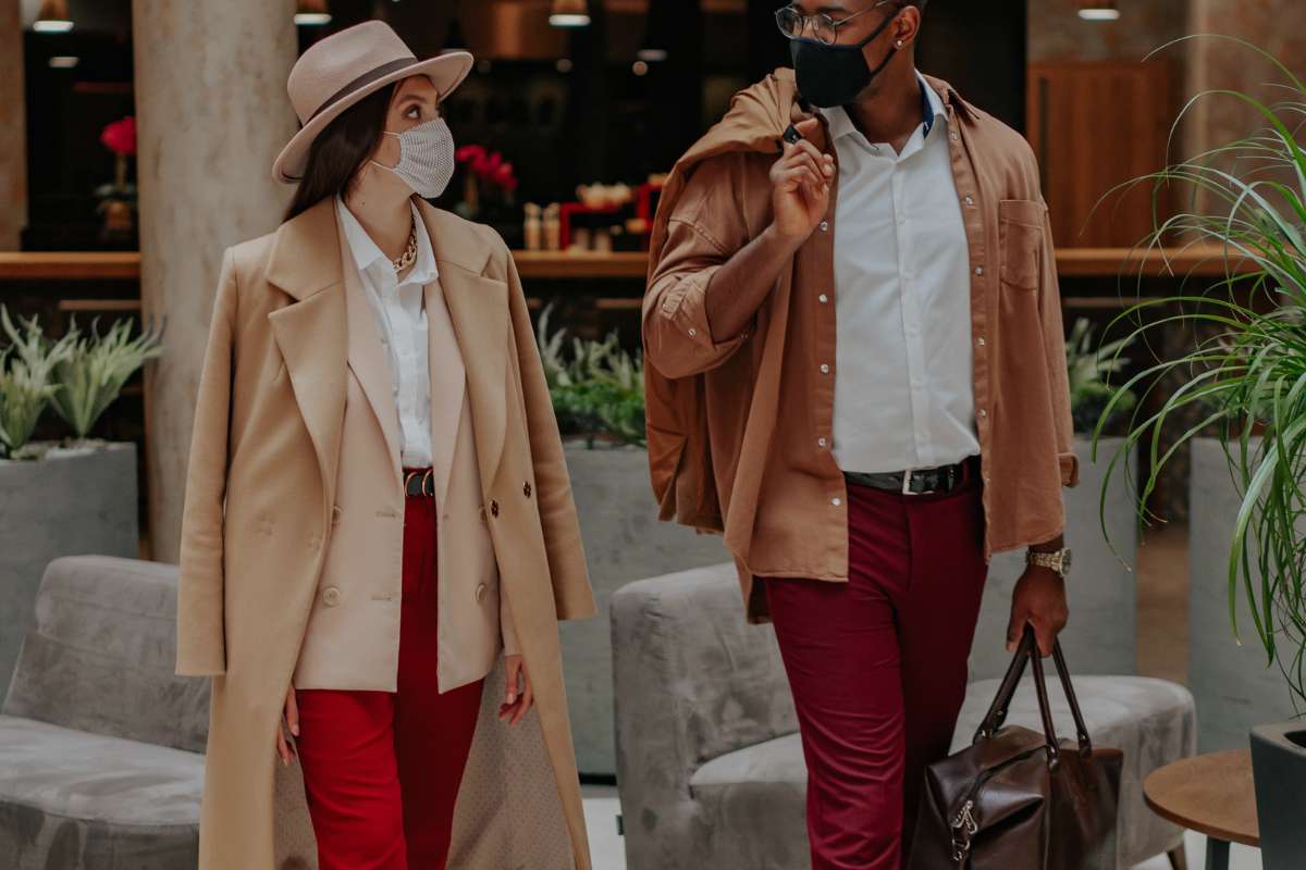 woman and man walking out of hotel lobby wearing face masks and carrying luggage