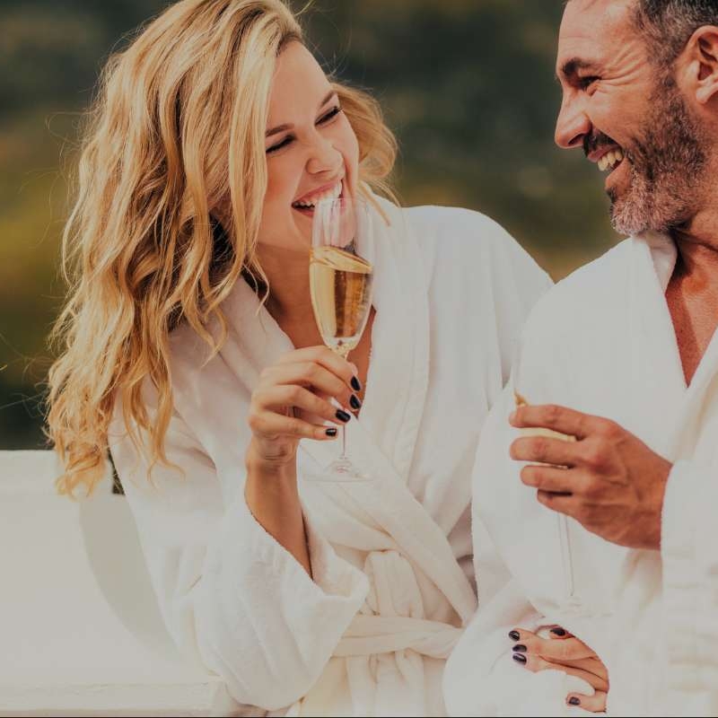 middle aged couple laughing while wearing robes and having champagne
