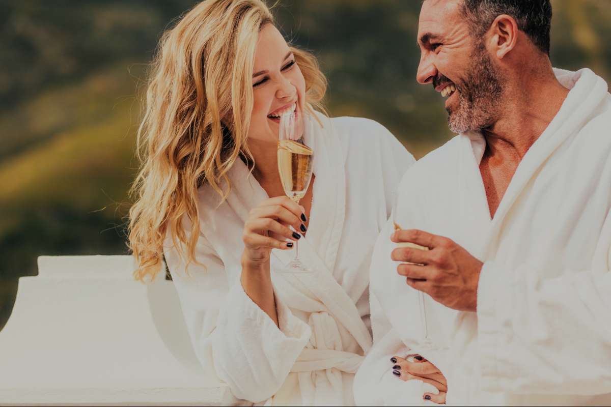 middle aged couple laughing while wearing robes and having champagne