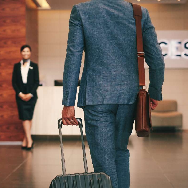 man in suit and roller suitcase walking into hotel lobby
