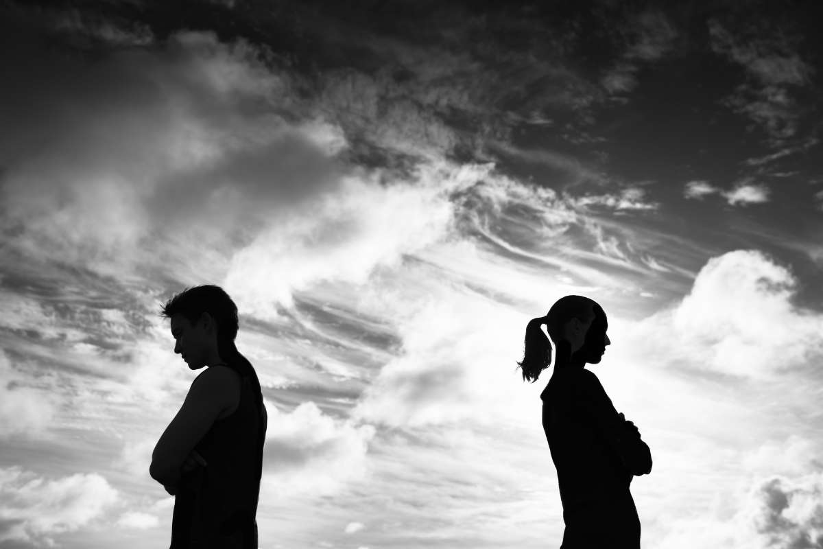 black and white photo of a man and woman standing with their backs to one another and a sky in the background