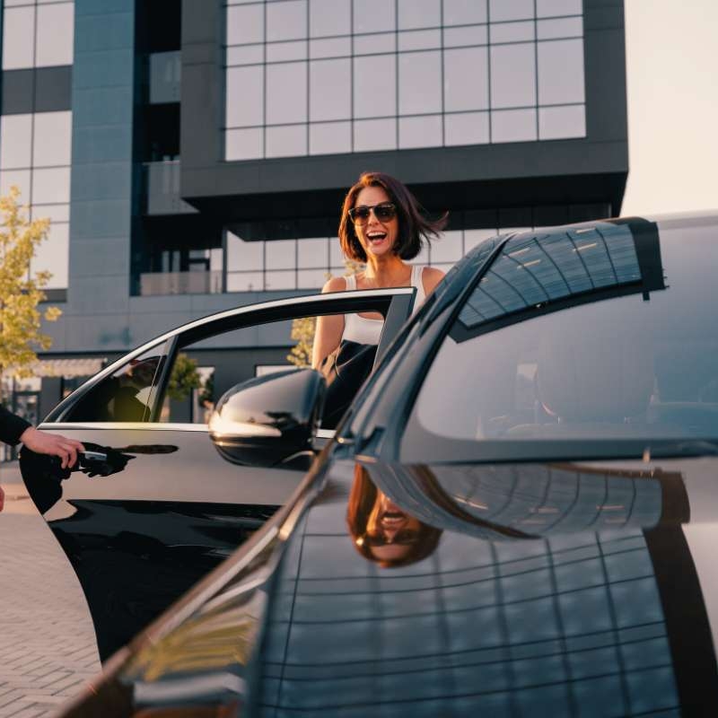 woman with sunglasses is smiling while exiting the back seat of black shiny car