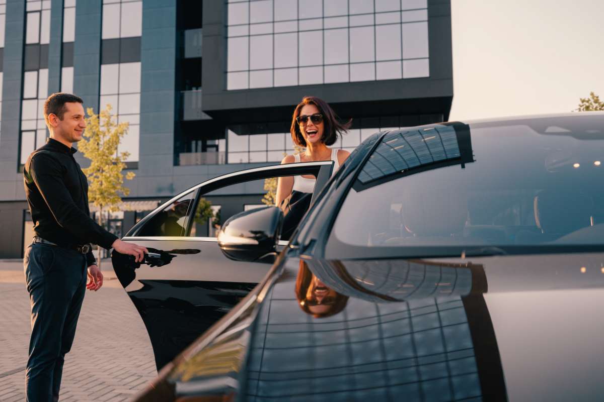 woman with sunglasses is smiling while exiting the back seat of black shiny car