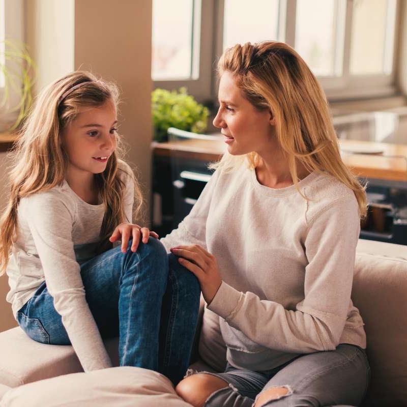 daughter sitting on couch with mom while mom touches daughter's knee