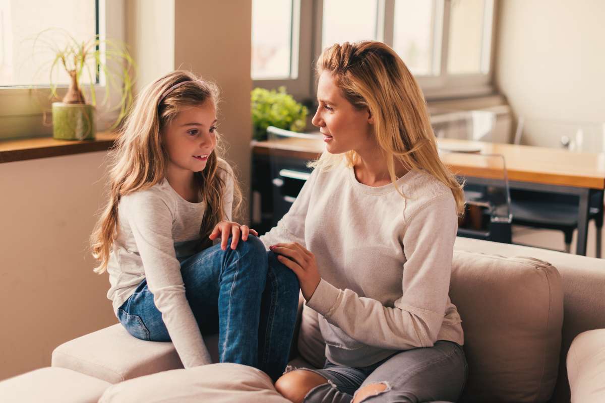 daughter sitting on couch with mom while mom touches daughter's knee