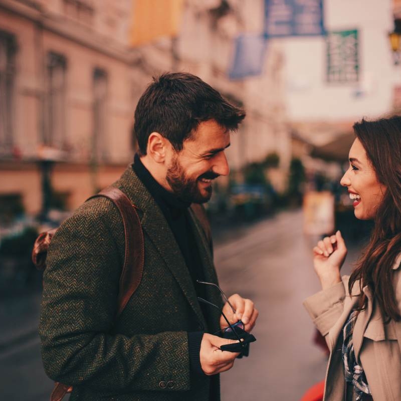 a man and woman talking outside a high rise. she is reacting positively to the personality traits he's displaying.