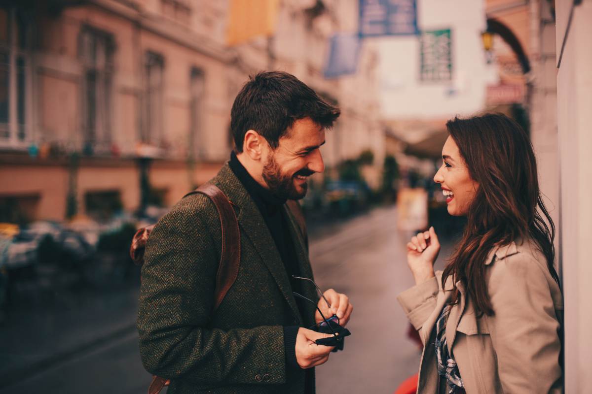 a man and woman talking outside a high rise. she is reacting positively to the personality traits he's displaying.