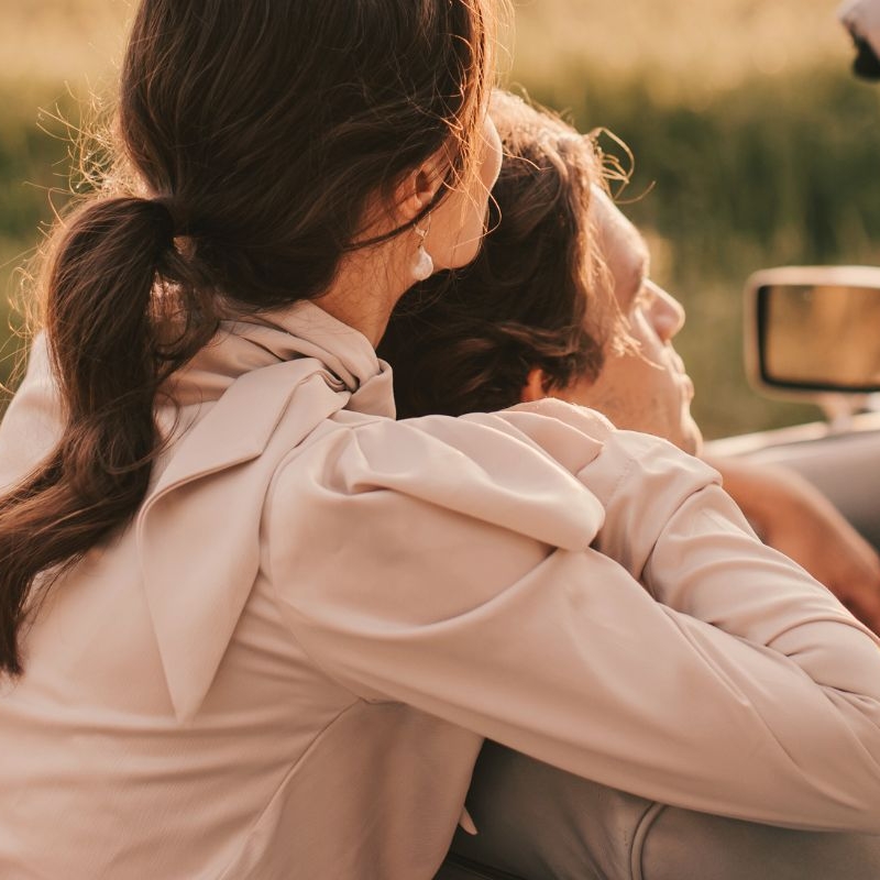 over-shoulder photo of a man and woman cuddling in a top-down convertible. this casual intimacy is one of the benefits of understanding your attachment in relationships.