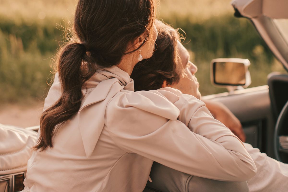 over-shoulder photo of a man and woman cuddling in a top-down convertible. this casual intimacy is one of the benefits of understanding your attachment in relationships.