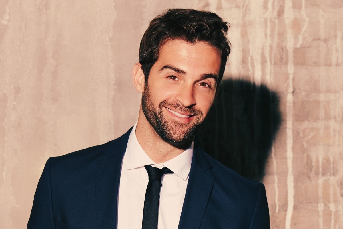 David smiling confidently in front of a light-colored wall. He is handsome and wearing a suit.