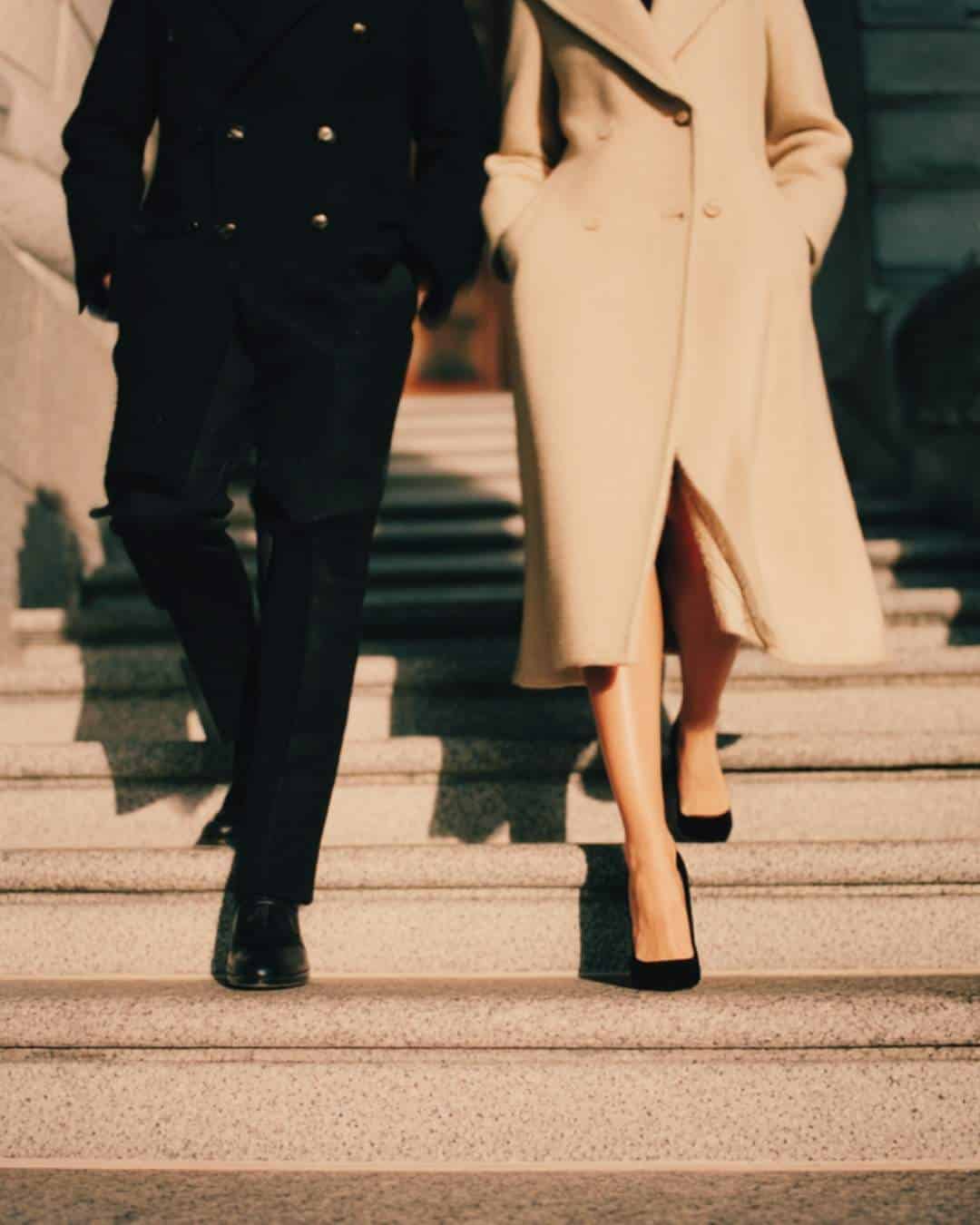 A man and woman in finely styled clothing walking down a stone staircase.